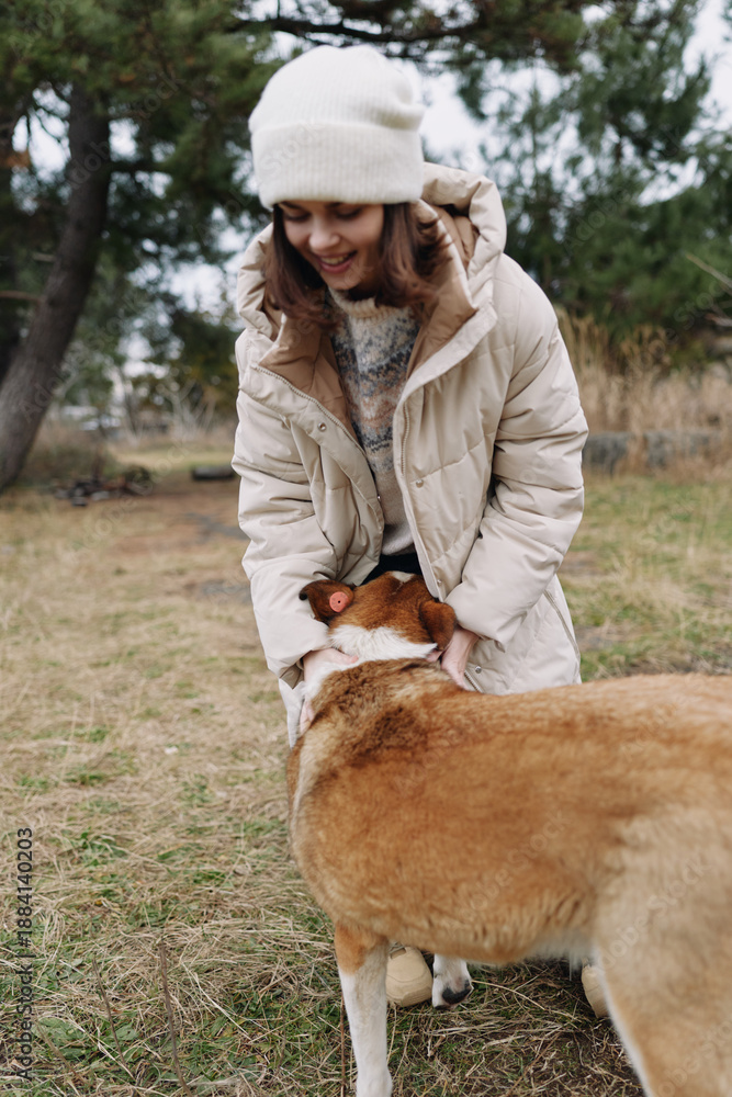 Fototapeta premium Woman in a warm coat and beanie crouches to greet a large dog, enjoying a playful moment outdoors in a park on a chilly day.