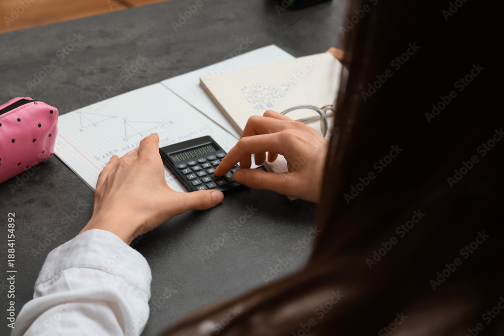 Obraz premium Woman using calculator and copybooks with math formulas on dark table, closeup
