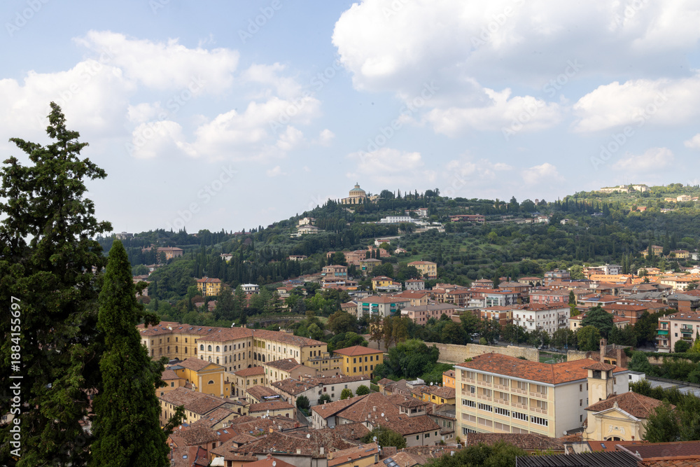 Fototapeta premium Photo of the beautiful city of Verona in Italy showing a view of houses and homes on the hillside that over looks the historical city on a sunny blue sky day with clouds in the sky