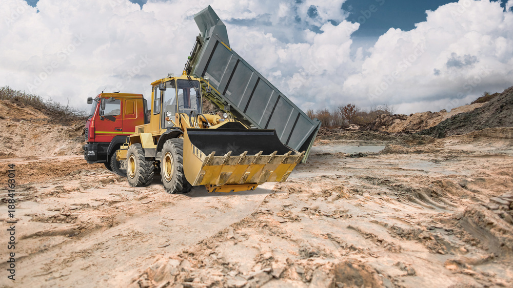 Fototapeta premium Heavy equipment works on a construction site with earthen embankments, against a backdrop of shifting clouds. A dump truck delivers earth, and a loader levels it