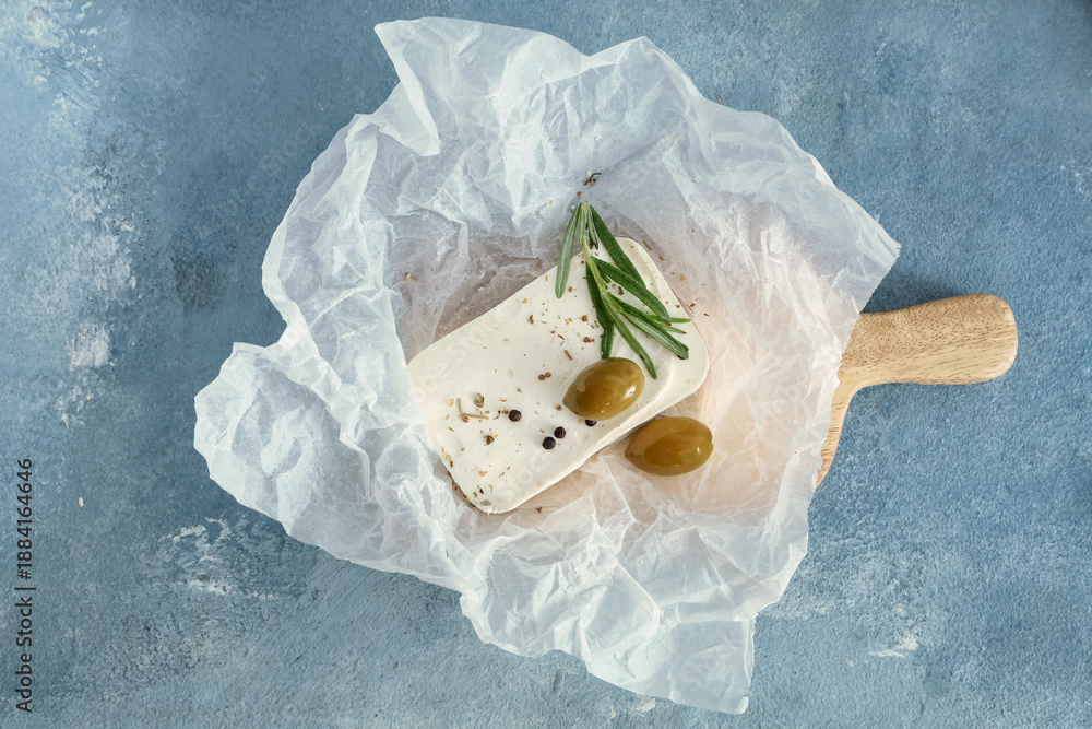 Fototapeta premium Paper with tasty feta cheese, olives, rosemary and peppercorn on blue background
