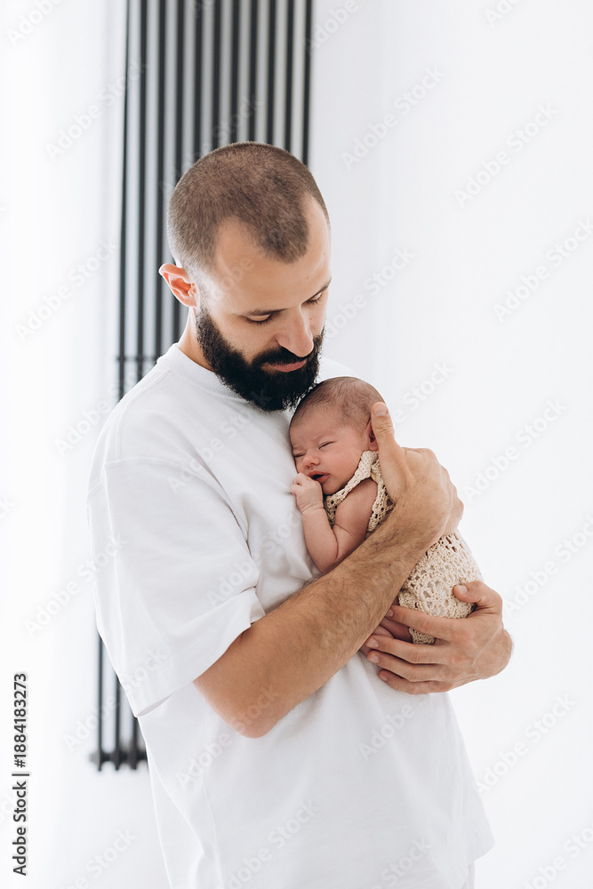 Φωτογραφία A father gently holds his newborn baby wrapped in a soft blanket, capturing a tender moment of care and love in a bright, minimalist room