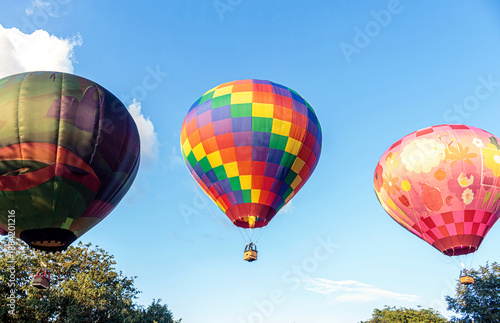 Three brightly colored hot air balloons, each with a different pattern, float together in the clear blue morning sky.