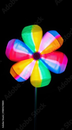 Vibrant rainbow LED flower pinwheel spinning in the dark with motion blur light trails. Psychedelic vertical video clip ideal for content creators on social media