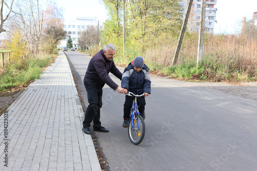 Man teaches a boy to keep balance on a bicycle on a quiet city street in autumn