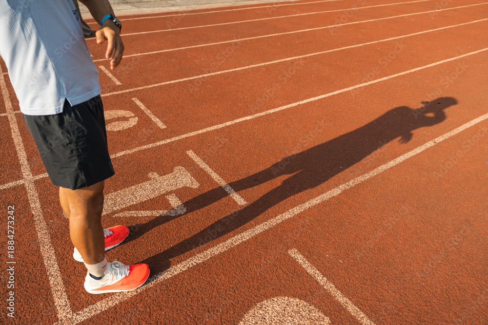 Naklejka premium Runner at track poised at the starting line casting shadow under the setting sun