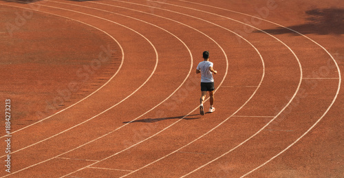Rear view of a runner in sportswear training on a red running track Athletic man sprinting
