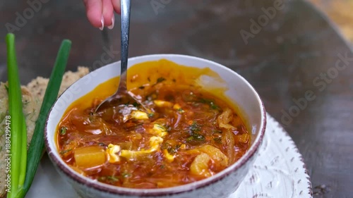 solyanka borscht adding sour cream to borsch soup on spoon. Woman stirring solyanka cream soup hodgepodge at table in home kitchen. High quality 4k footage