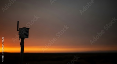 A silhouette of an outdoor environmental sensor monitoring air quality with a smoke detector, set against a wildfire smoke filled sunset background. Perfect for environmental reports,