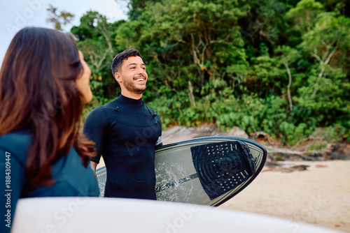 Photography Young man and woman on a tropical beach, wearing wetsuits and carrying surfboard