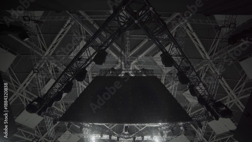 Massive dark LED panel hangs above stage in triangular frame. Grid structure supports lights and forms core of concert equipment setup