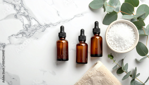Minimalist flat lay of amber glass dropper bottle, eucalyptus leaf, bath salt, towel on white marble, spa essentials for relaxation and wellness, natural skincare concept