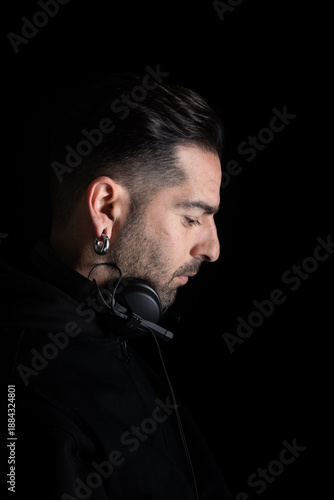 The DJ is concentrating on the music while wearing headphones. The setting is dark, emphasizing the DJ's profile. There is a sense of dedication to the craft in this moment.