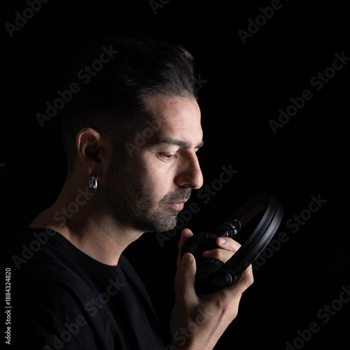 A DJ is seen holding a pair of headphones up close to his face. He appears deep in thought as he prepares for the next track.
