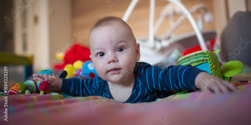 Little sprout exploring the world from the nursery floor, surrounded by playful toys. A small baby lies on a colorful play mat, reaching for toys and observing the room