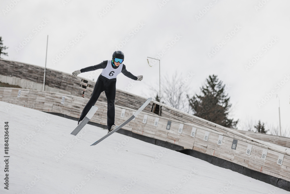 Fototapeta premium Athlete performing a ski jump during a training session on a ski jump hill, showcasing aerial technique and athletic skill.