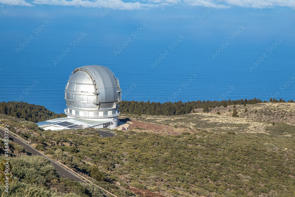 Obraz premium Side view of the Gran Telescopio Canarias dome in La Palma, situated on a high volcanic plateau above the clouds and the Atlantic Ocean, surrounded by native high-altitude vegetation.