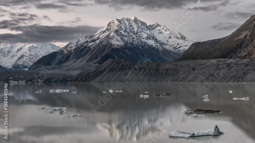 Last light of day at Tasman Glacier with snow-capped mountains, floating icebergs and moody clouds