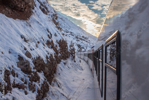 Eastern Express train curving through snowy Erzincan mountains. Features red locomotive, white winter landscape, and scenic window reflections. Iconic Turkish rail journey in Eastern Anatolia.