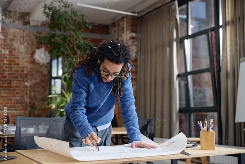 Canvas-taulu Young adult Black man standing at desk reviewing architectural blueprints, leani