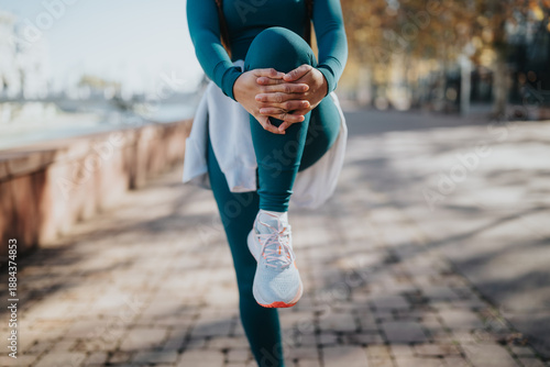 Tableau sur toile A person in teal active wear lifts a knee in a balanced stretch outdoors