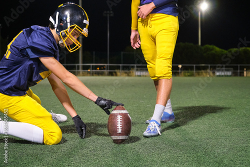 American football player preparing game, holding ball on a green turf field at night