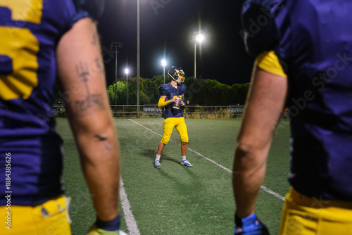 Player standing on an illuminated stadium field at night, holding a football