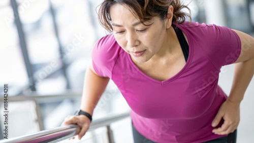 middle aged woman climbing stairs with visible difficulty while holding her hip, illustrating joint pain, mobility issues and everyday physical challenge
