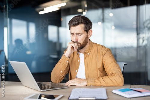 Foto Businessman sitting at office desk, looking troubled and focused on his laptop,