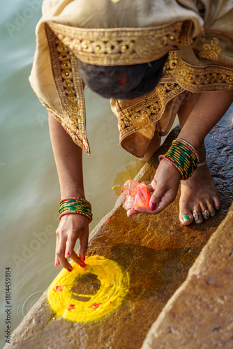 India. Uttar Pradesh State. Varanasi. A richly adorned young Hindu pilgrim, dressed in a golden sari, makes a ritual offering of haldi (turmeric) powder during the Diwali celebrations