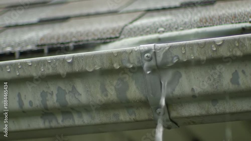 Rainwater flows down a l gutter attached to a roof during a storm.
