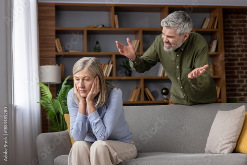 Obraz na plátně Senior man yelling at frustrated mature woman sitting on sofa, depicting relatio