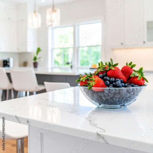 A clear glass bowl of fresh strawberries and blueberries on a bright kitchen island.
