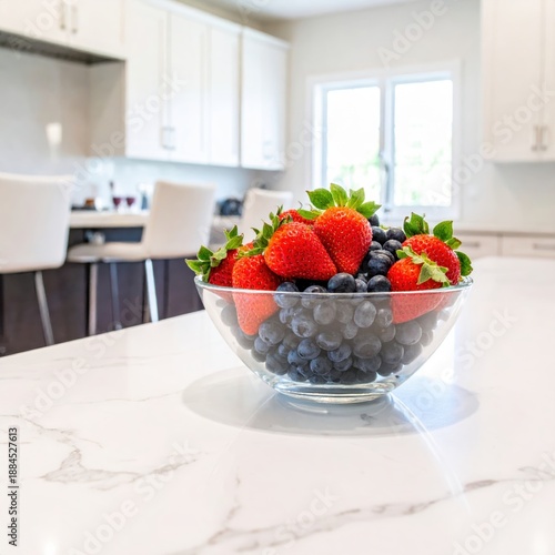 A vibrant glass bowl brimming with fresh strawberries and blueberries sits on a sleek kitchen counter.
