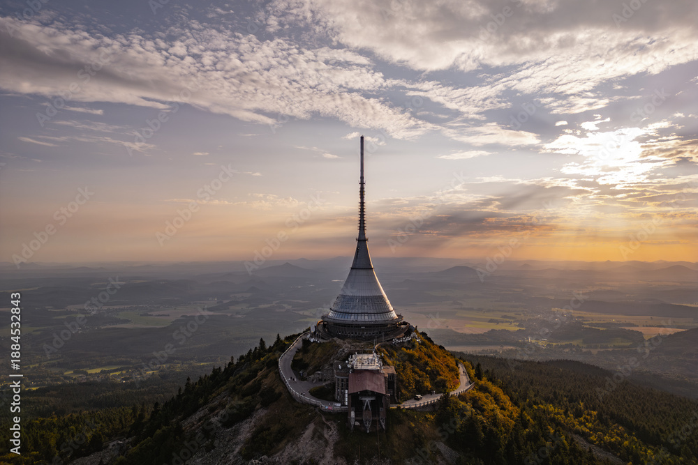 Naklejka premium Jested Mountain Hotel stands majestically on a hilltop in Liberec, showcasing its modern architecture against a backdrop of a beautiful sunset. The evening light enhances the scenic views.