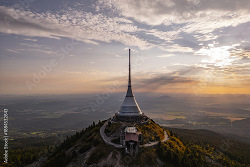 Jested Mountain Hotel stands majestically on a hilltop in Liberec, showcasing its modern architecture against a backdrop of a beautiful sunset. The evening light enhances the scenic views.