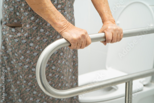 Asian elderly woman use toilet security support rail in bathroom.