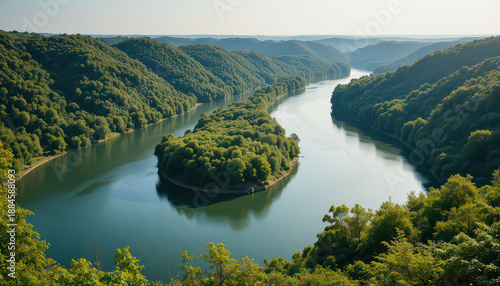 Majestic aerial view captures a serpentine river meandering through deep, lush green forested valleys under bright morning sunlight creating serene natural beauty.