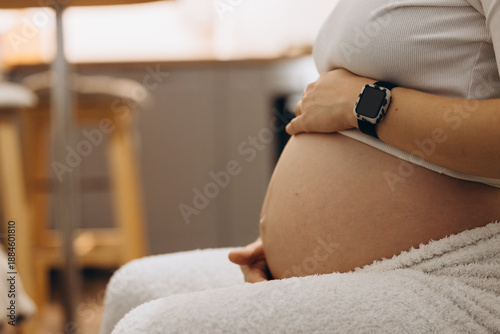 Close-Up Of Pregnant Belly With Smartwatch On Wrist, Symbolizing Health Monitoring During Pregnancy. Concept Of Modern Motherhood, Prenatal Care, Technology And Wellness, And Maternity Lifestyle. Soft