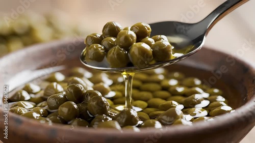 Closeup view of fresh green capers being scooped from a rustic wooden bowl with a silver spoon highlighting the briny tangy flavor and their use as a gourmet ingredient in Mediterranean cuisine and v.