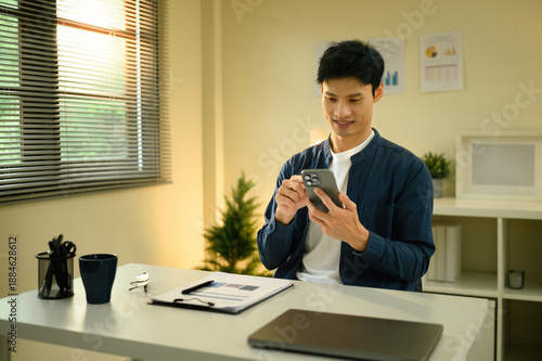 Entrepreneur managing digital tasks on his mobile phone in a bright and comfortable home office