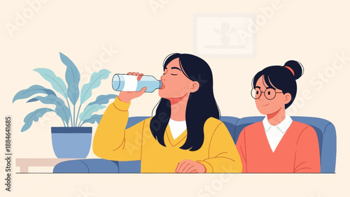 Two young women relax on a sofa, one drinks water from a bottle