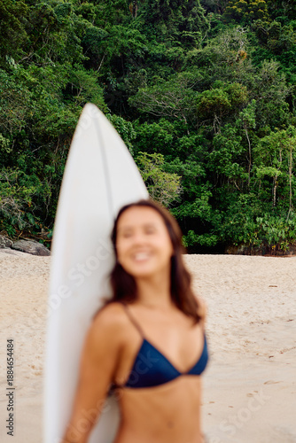 Canvas Print Young woman standing on a sandy beach holding a surfboard, smiling and relaxing