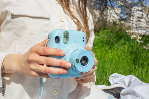 Smiling young woman holding instant camera at picnic on green grass