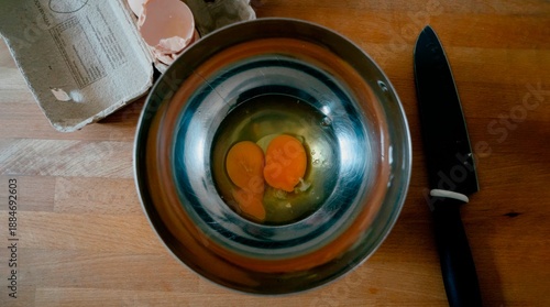 Raw eggs in metal bowl on wooden table, breakfast preparation ingredients, top view flat lay, home cooking concept, simple kitchen scene