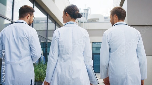 Wallpaper Mural Focused female doctor holding folders and walking between two male colleagues. Confident team moving together and discussing upcoming duties. Professionals continuing route toward clinic entrance. Torontodigital.ca