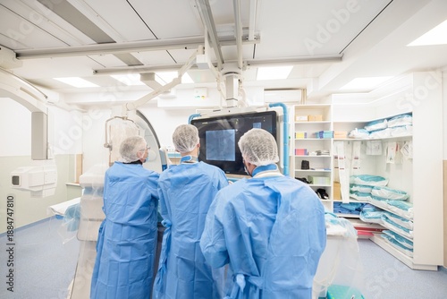 Three medical professionals in blue scrubs collaborate in a sterile environment, using advanced technology to conduct a vital endovascular procedure