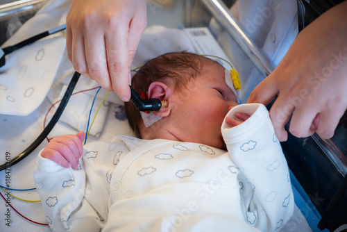 Newborn baby receiving a hearing screening test by medical professional in a hospital, assessing infant auditory health and developmental well-being at early age
