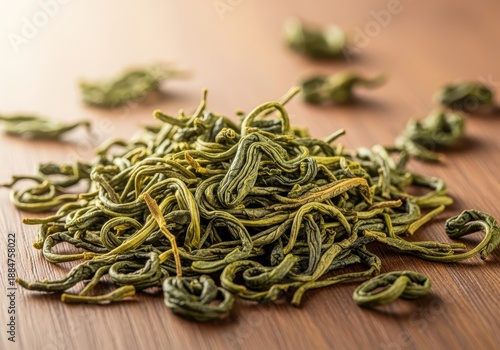 A close-up view of aromatic dried green tea leaves scattered on a wooden surface, ready to be measured for brewing a hot beverage, harvest, leaves, caffeine