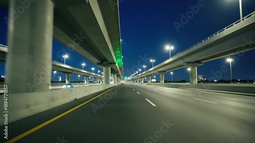 A nighttime view of a multilevel highway with streetlights and a clear blue sky, showing a road with yellow lines and white markings